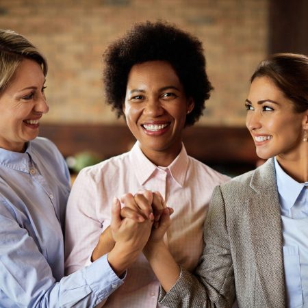Happy black businesswoman holding hands in unity with her female colleagues and looking at camera.
